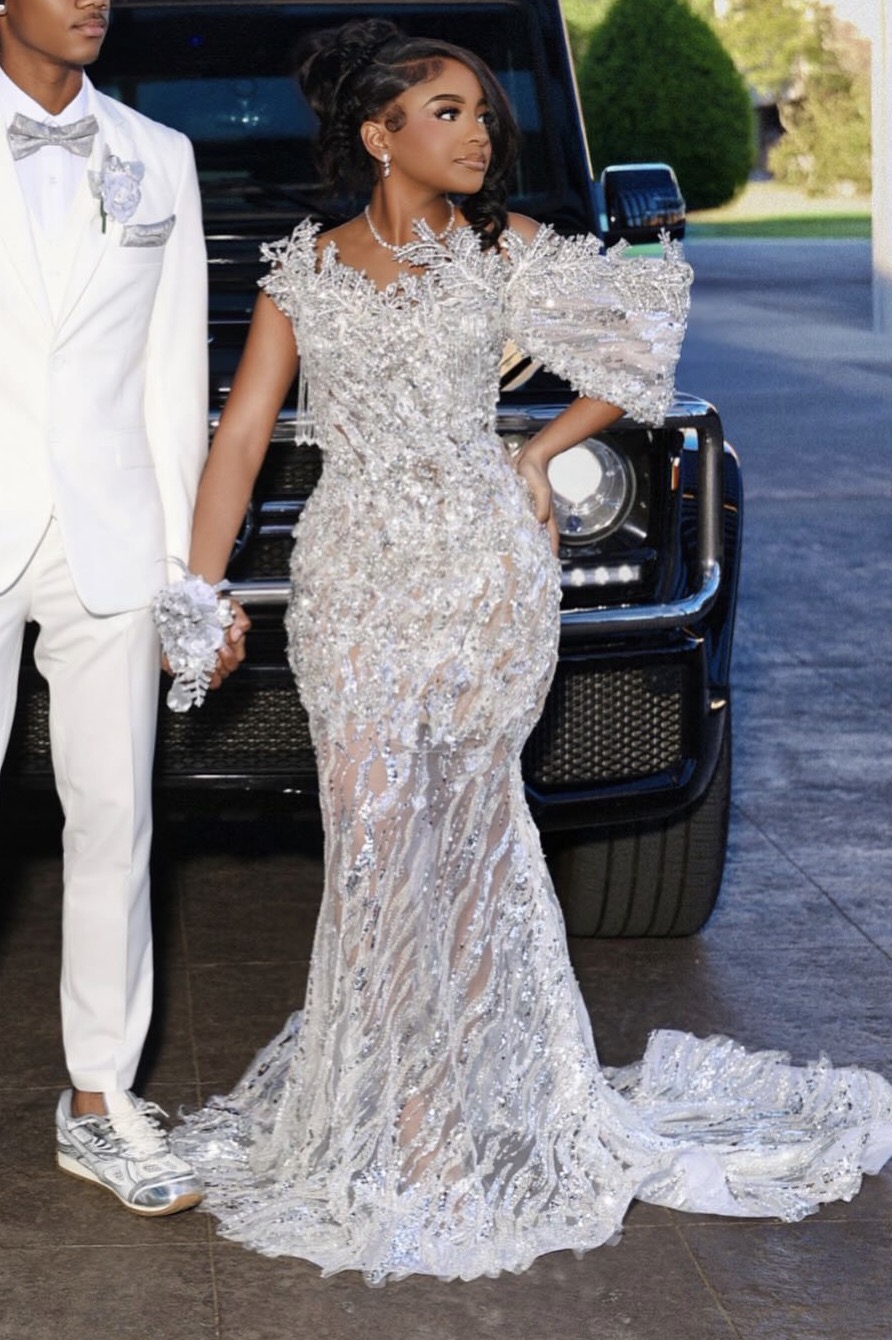 Prom couple in custom silver beaded gown beside SUV